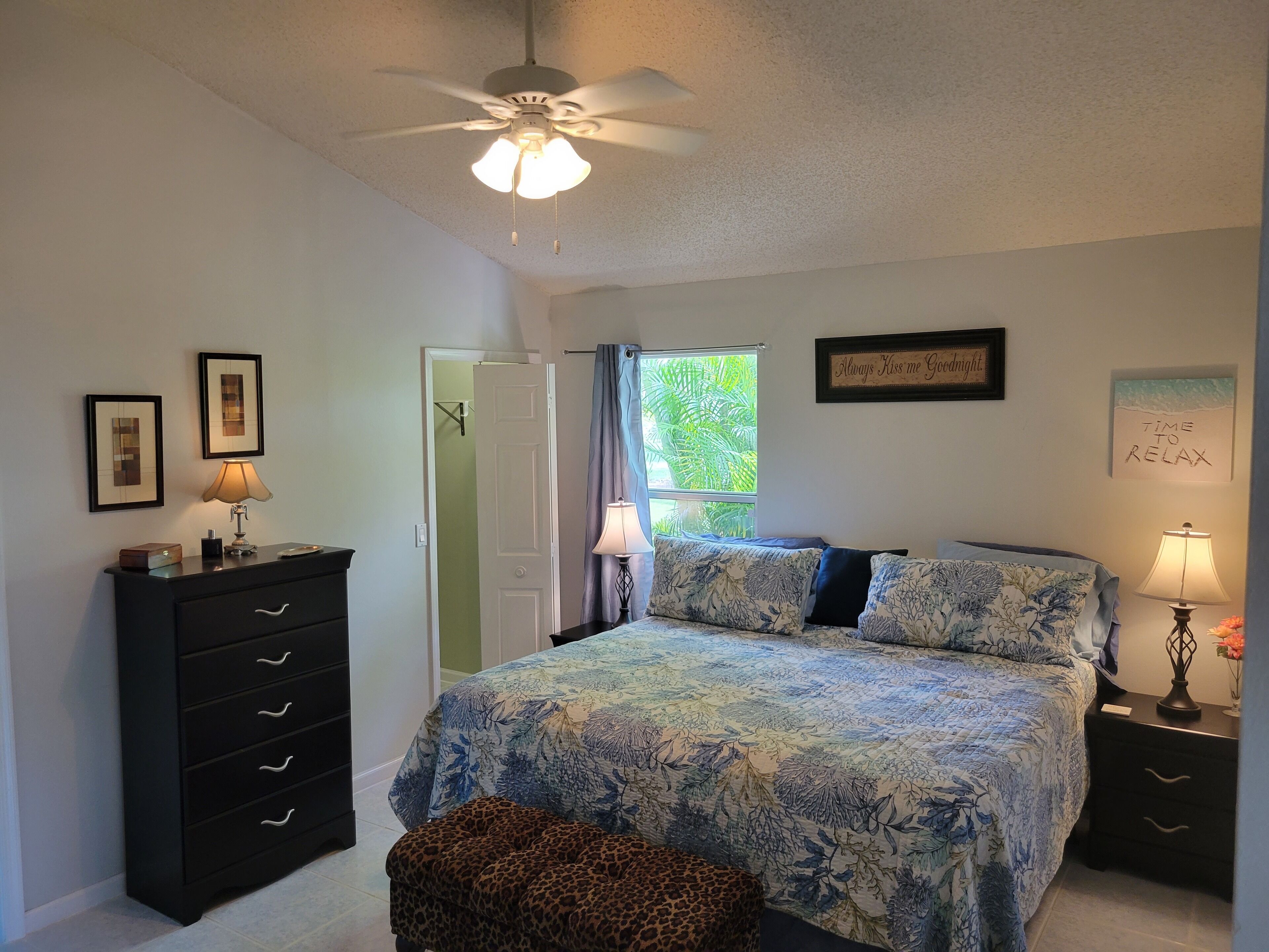 A bedroom with a bed, a ceiling fan, a dresser, a nightstand, and a window with curtains.