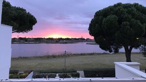 Vista de un lago con atardecer, árboles y un edificio blanco.