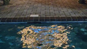 Un área de bar al aire libre con una pantalla de televisión, luces colgantes y una piscina.