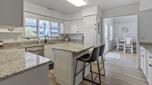 Una cocina moderna con armarios blancos, encimeras de granito y una isla central con taburetes de bar.