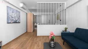 Ein modernes Interieur mit Holzboden, einem blauen Sofa, einem schwarzen Tisch mit Blumen und einer weißen Trennwand mit vertikalen Lamellen.