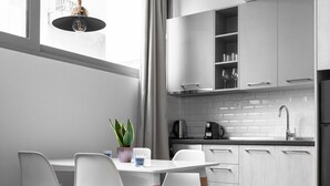 Eine moderne Küche mit weißen Schränken, einem Essbereich mit weißem Tisch und Stühlen sowie einer hängenden Leuchte.