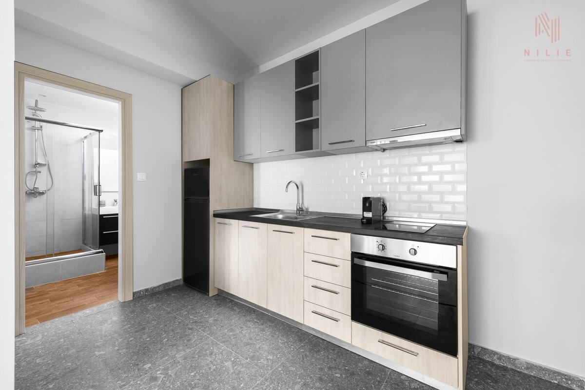 A modern kitchen with a black oven, stainless steel sink, and light wood cabinets.