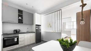 Eine moderne Küche mit weißen Schränken, einem schwarzen Kühlschrank und einem Essbereich mit weißem Tisch und einer Pflanze.