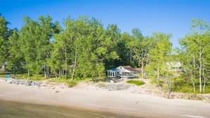 A beachfront property with a covered patio, surrounded by trees and a sandy beach.