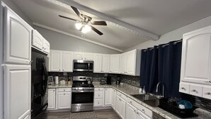 A modern kitchen with white cabinetry, stainless steel appliances, a microwave, stove, and a ceiling fan.