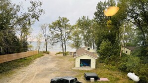 A beach house with a garage, a covered deck, and a dirt path leading to the beach.