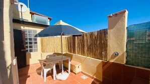 Un pequeño patio con una mesa, sillas, un paraguas azul y una cerca de bambú.