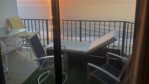A balcony with a glass table, two chairs, and a lounge chair facing the ocean at sunset. - The Plaza - Direct Oceanfront  Luxury Condo with Beach bar-Discount weekly  (Ocean City)