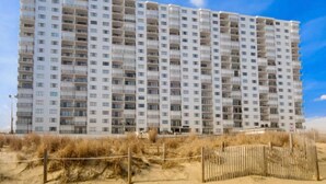 A multi-story hotel with a uniform exterior, balconies, and a sandy beach in the foreground. - The Plaza - Direct Oceanfront  Luxury Condo with Beach bar-Discount weekly  (Ocean City)