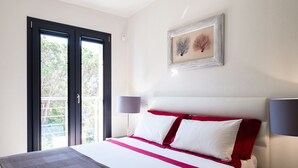 A hotel room with a bed, a nightstand, a lamp, and a window with a view of trees.