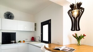 A modern kitchen with white cabinets, a black coffee machine, and a wooden dining table with a magazine.