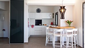 A modern kitchen with white cabinets, a black countertop, and a wooden dining table with white chairs.