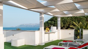 Eine Dachterrasse mit Blick aufs Meer, weiße Liegestühle und ein kleiner Tisch mit Obstschale.
