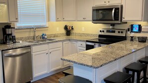 Una cocina moderna con gabinetes blancos, encimera de granito, lavavajillas de acero inoxidable, microondas, estufa y ventilador de techo.