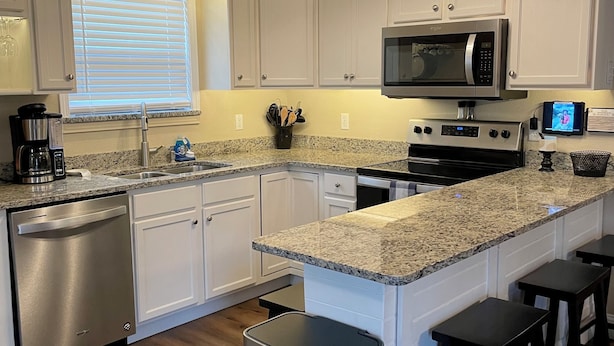 A modern kitchen with white cabinets, a granite countertop, a stainless steel dishwasher, a microwave, a stove, and a ceiling fan. - Lakefront Cabin : Boat Slip : Dock : Kayaks : Families : Internet (Jacksboro)