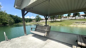A concrete dock with a wooden swing bench overlooking a calm lake, surrounded by trees and a stone wall. - Lakefront Cabin : Boat Slip : Dock : Kayaks : Families : Internet (Jacksboro)
