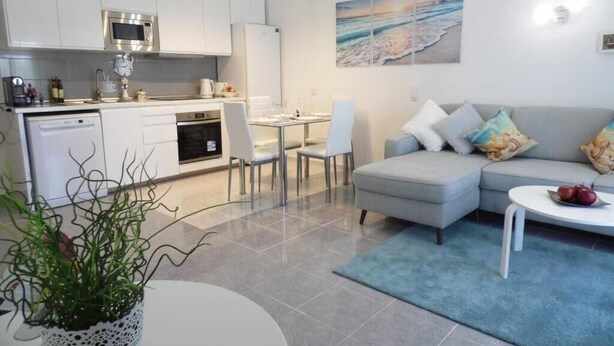 A modern kitchen with white cabinets, a microwave, and a dishwasher. There is a dining area with a table and chairs, and a living area with a sofa and a coffee table.
