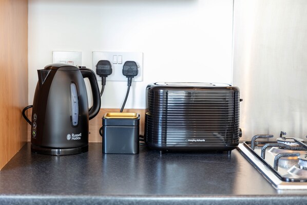 Una encimera de cocina con una cafetera, un tostador y un pequeño electrodoméstico, todo conectado.