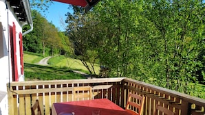 Een tafel buiten gedekt met een rode tafelkleed, omringd door houten stoelen, met uitzicht op een weelderig groen landschap en een pad.