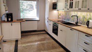 Een keuken met witte kastjes, een zwart aanrecht, een raam met zonwering, een inbouwoven en een magnetron.