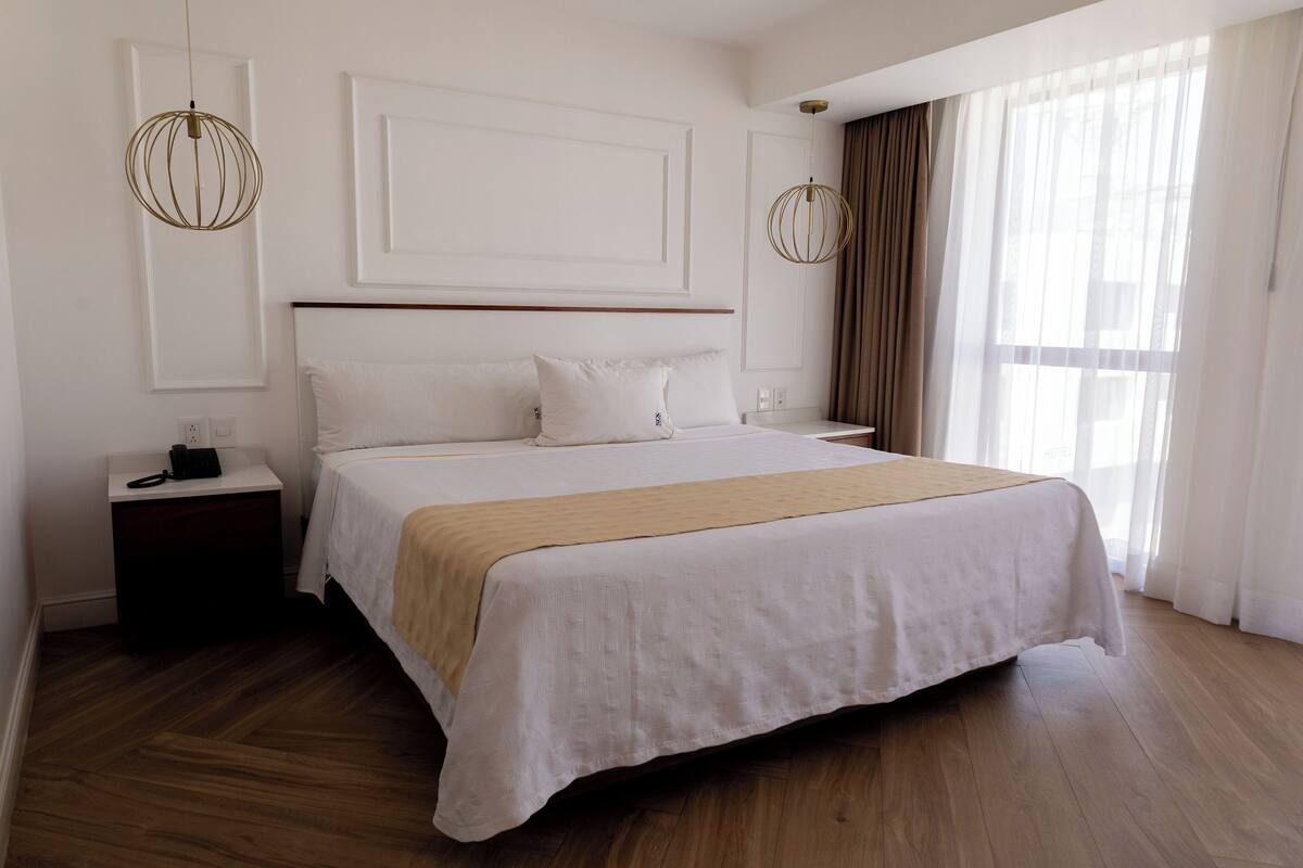Una habitación de hotel con una cama grande, una mesita de noche con teléfono y una ventana con cortinas.