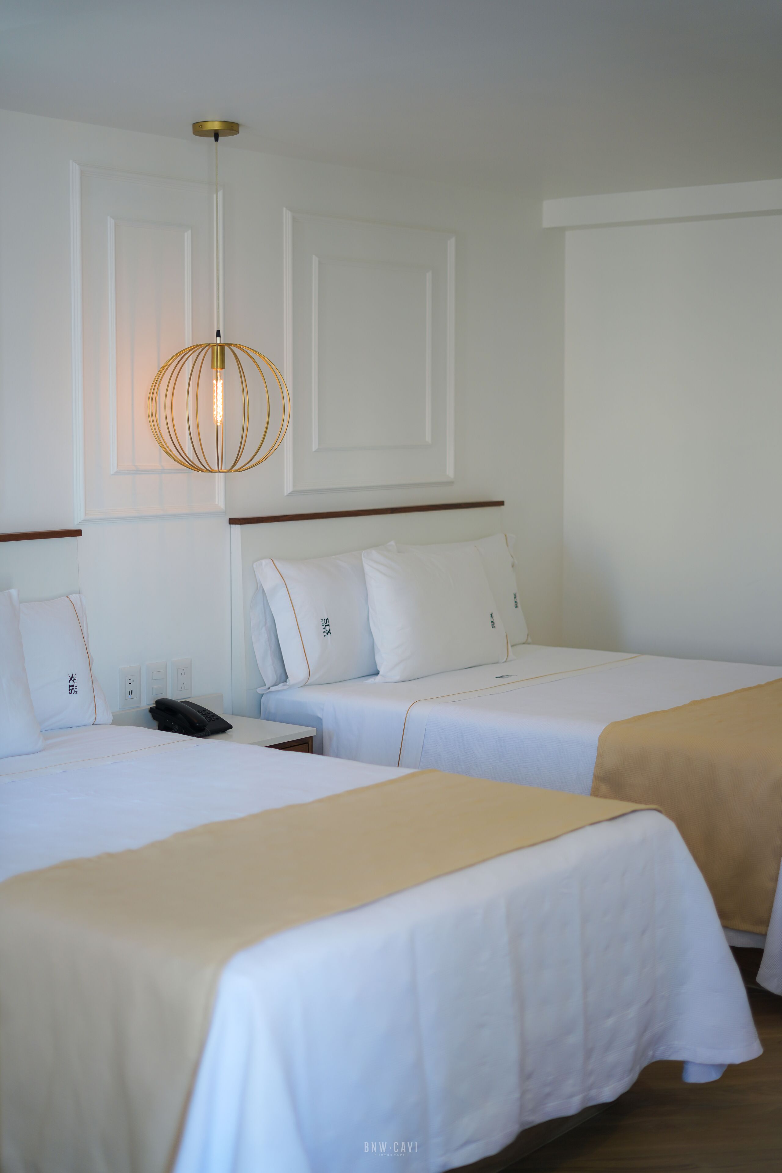 Une chambre d’hôtel avec deux lits simples, une table de chevet avec un téléphone et un luminaire suspendu.