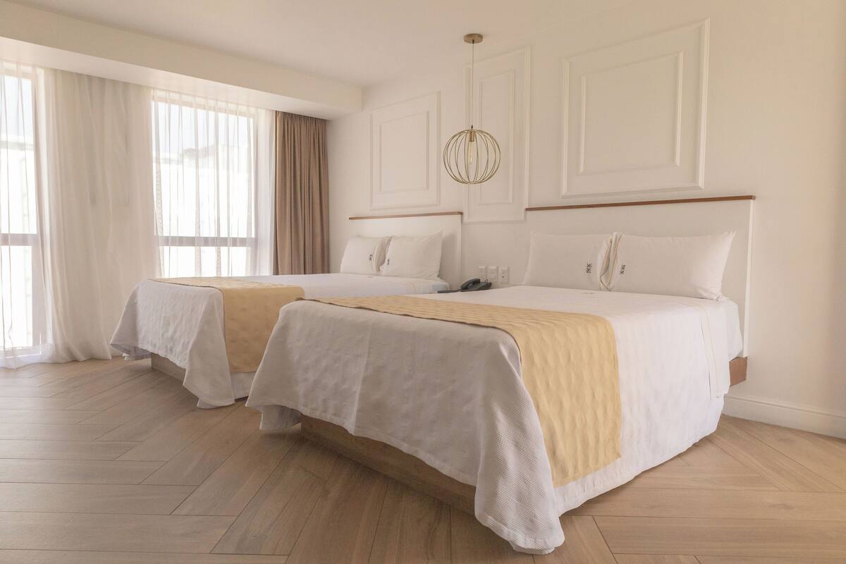 Habitación de hotel con dos camas, piso de madera y un ventanal con cortinas.