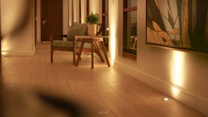 Un pasillo con piso de madera, una silla, una mesita con una planta y un cuadro en la pared.