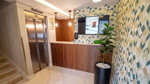 Zona de recepción de un hotel con diseño moderno, que incluye un mostrador de recepción, un espejo grande y una planta en maceta.