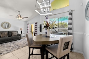 A dining area with a table and chairs, a ceiling fan, and a view through a window with curtains. - 463 -4 bedroom villa with south facing private pool & Spa (Kissimmee)