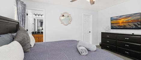 Un dormitorio con cama, ventilador de techo, cómoda, espejo y un cuadro en la pared.