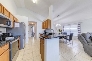 A modern kitchen with a central island, wooden cabinets, and a dining area with a gray sofa.