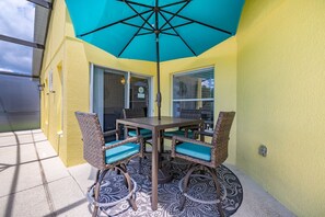 An outdoor patio with a table and chairs, a blue umbrella, and a patterned rug. - 463 -4 bedroom villa with south facing private pool & Spa (Kissimmee)