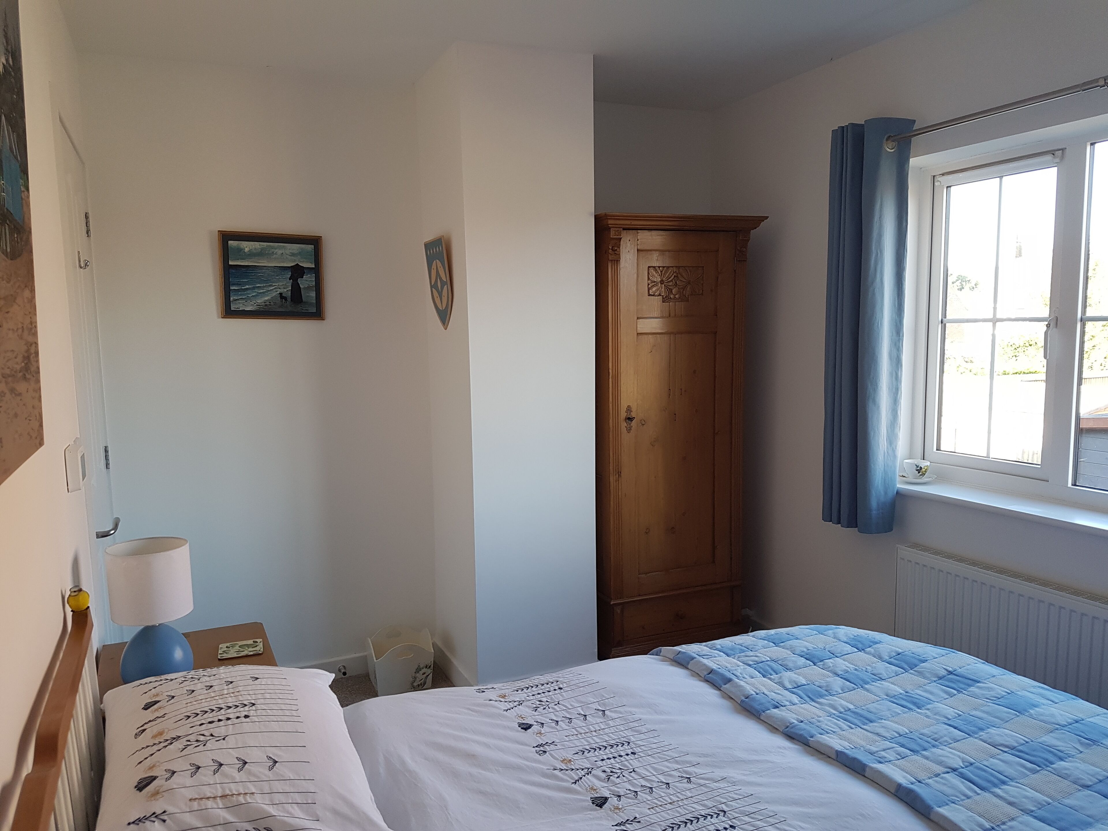 A bedroom with a bed, a wooden wardrobe, a window with curtains, and a wall with a painting.