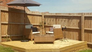 Eine Holzterrasse mit Korbmöbeln, einem Sonnenschirm und einem kleinen Tisch mit einer Flasche.