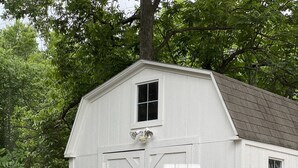 A white wooden shed with two doors and a small window, surrounded by trees and a gravel path. - Tempurpedic beds, walk to food, play ping pong & fenced artificial turf yard (Austin)