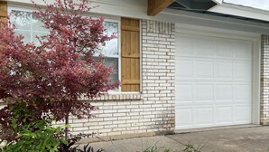 A residential garage with a white garage door, a brick exterior, and a window with wooden shutters. - Tempurpedic beds, walk to food, play ping pong & fenced artificial turf yard (Austin)