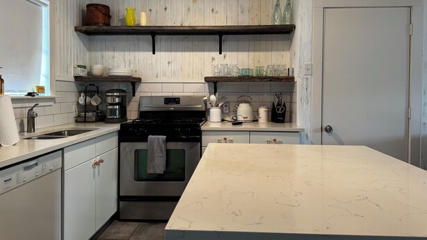 A kitchen with white cabinetry, a stove, a coffee maker, and shelves with glassware. - Tempurpedic beds, walk to food, play ping pong & fenced artificial turf yard (Austin)