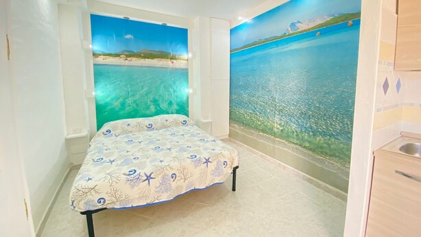 Ein Schlafzimmer mit Bett, Wandbild mit Strandmotiv und einem kleinen Badezimmerbereich.