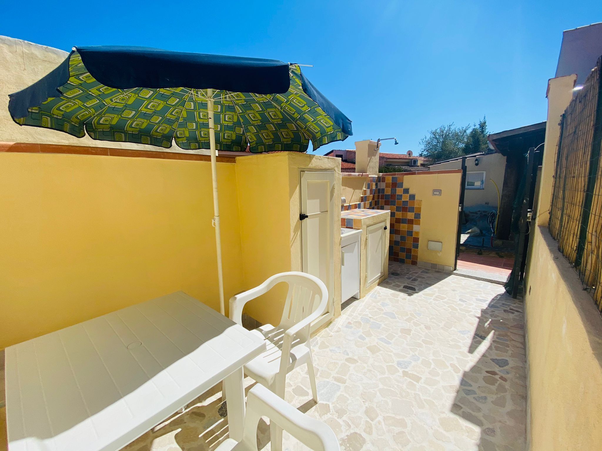 Un pequeño patio al aire libre con una mesa, sillas, un paraguas estampado y una pared de azulejos.