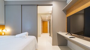 A modern hotel room with a bed, a flat-screen TV, a desk, and a bathroom visible through an open door. - Apto Completo no Eco Resort (Rio Formoso)