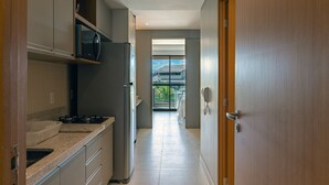 A modern kitchen with a gas stove, microwave, and refrigerator. A sliding glass door leads to a balcony with a view of the sky and greenery. - Apto Completo no Eco Resort (Rio Formoso)