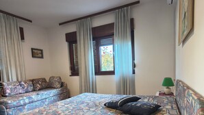 A room with a bed, a sofa, a window with curtains, and a wall-mounted air conditioner.