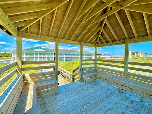 Une terrasse en bois avec des bancs, un espace abrité doté d’un toit en pente, et une vue sur un immeuble avec de nombreux balcons.