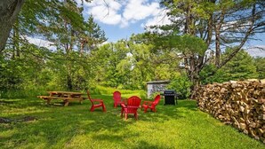 A picnic area with a wooden table and red chairs, surrounded by a stone wall and trees. - Modern 2 Bedroom with Outdoor Space (Ithaca)
