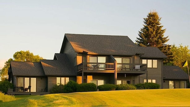 A two-story house with a balcony on the second floor, surrounded by a well-maintained lawn and a large tree.