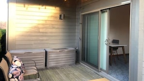 A patio with a wooden deck, a seating area with cushions, and a sliding glass door leading to an interior room with a table and chairs.