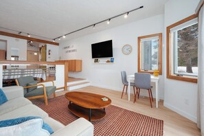 A modern living room with a sofa, coffee table, and dining area. - Golf course view, close to the beach (Cedar)