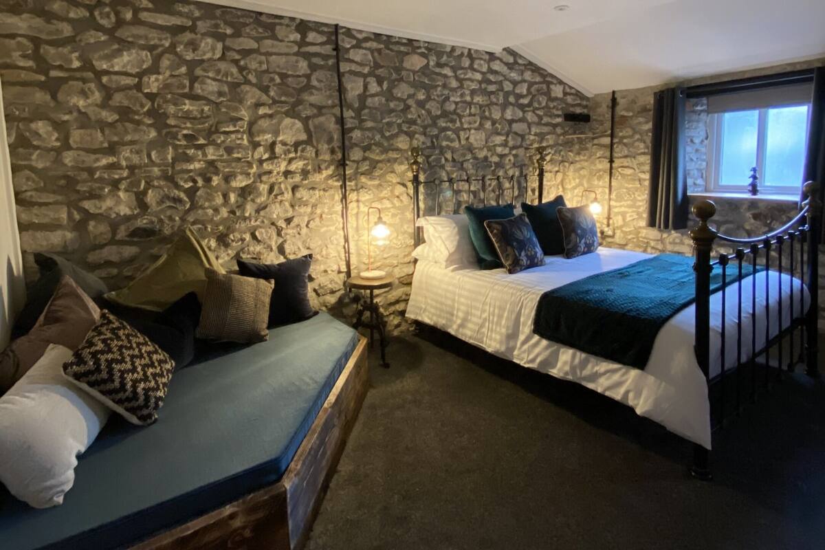 Un dormitorio con pared de piedra, dos camas, una mesita de noche y una ventana con vistas.
